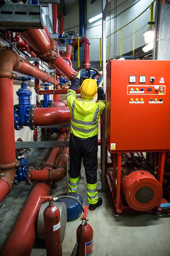 Industrial worker in safety gear inspecting machinery in a control room, highlighting workplace injury management gaps such as inadequate training, safety protocols, and emergency preparedness.